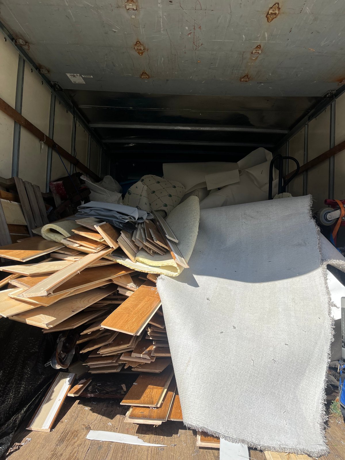 Interior of a truck bed loaded with furniture, wooden pieces, bedding, and household items ready for moving or transport