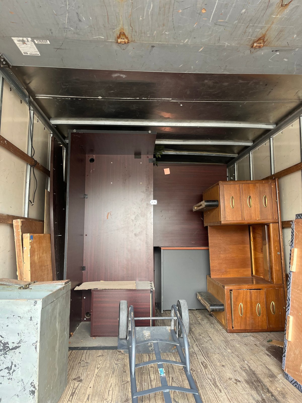 Interior of empty moving truck with wooden furniture, metal hand truck, and steel ceiling panels