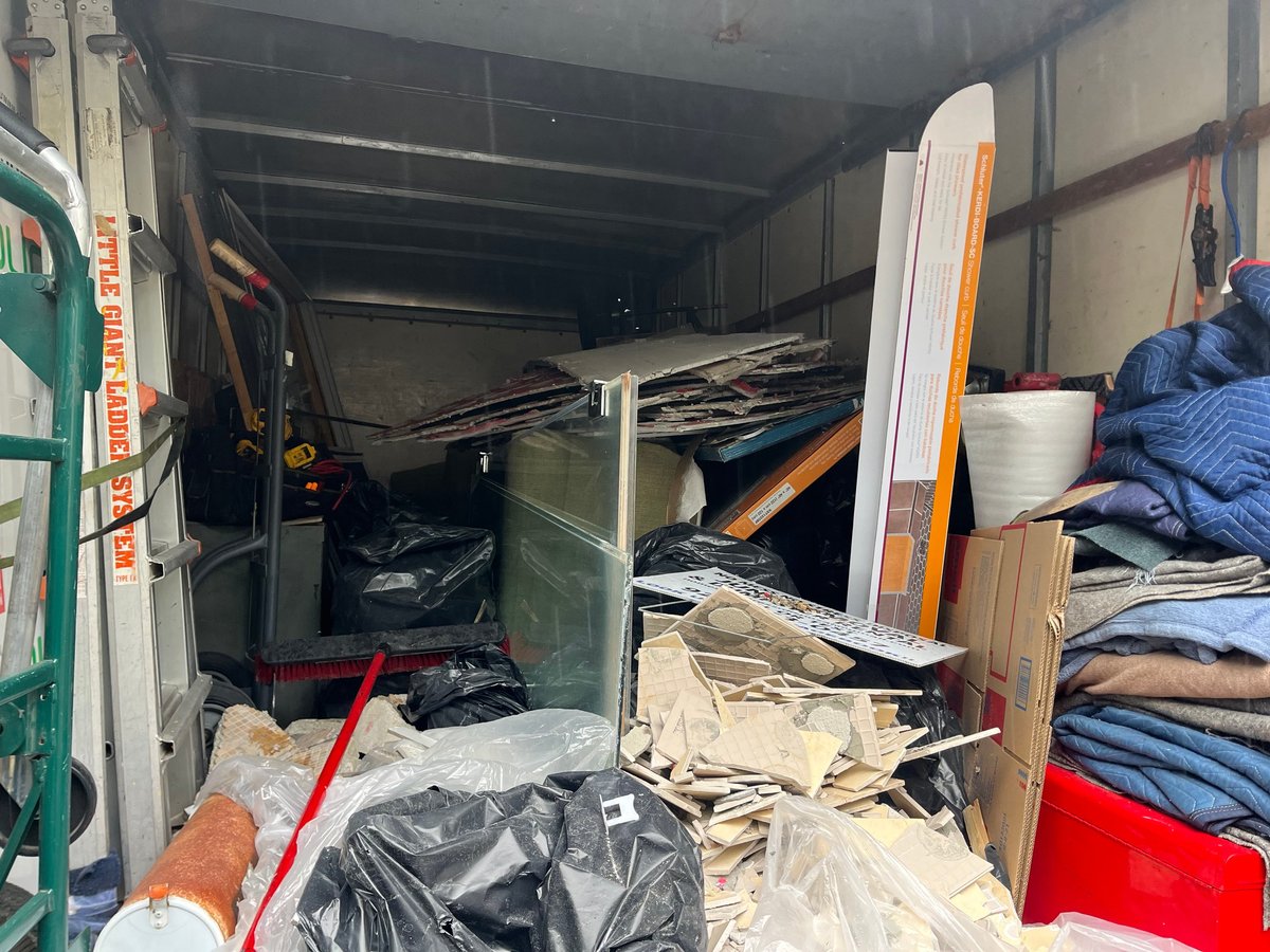 Packed moving truck interior filled with boxes, furniture, clothing, and household items stacked haphazardly